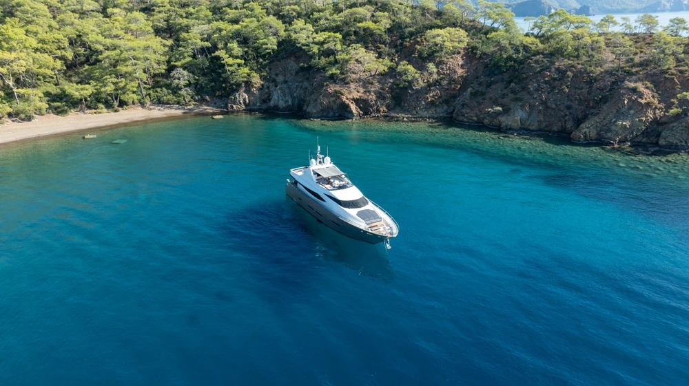 Yacht at anchor by the Maldives in deep turquoise water with greenery of the island behind.